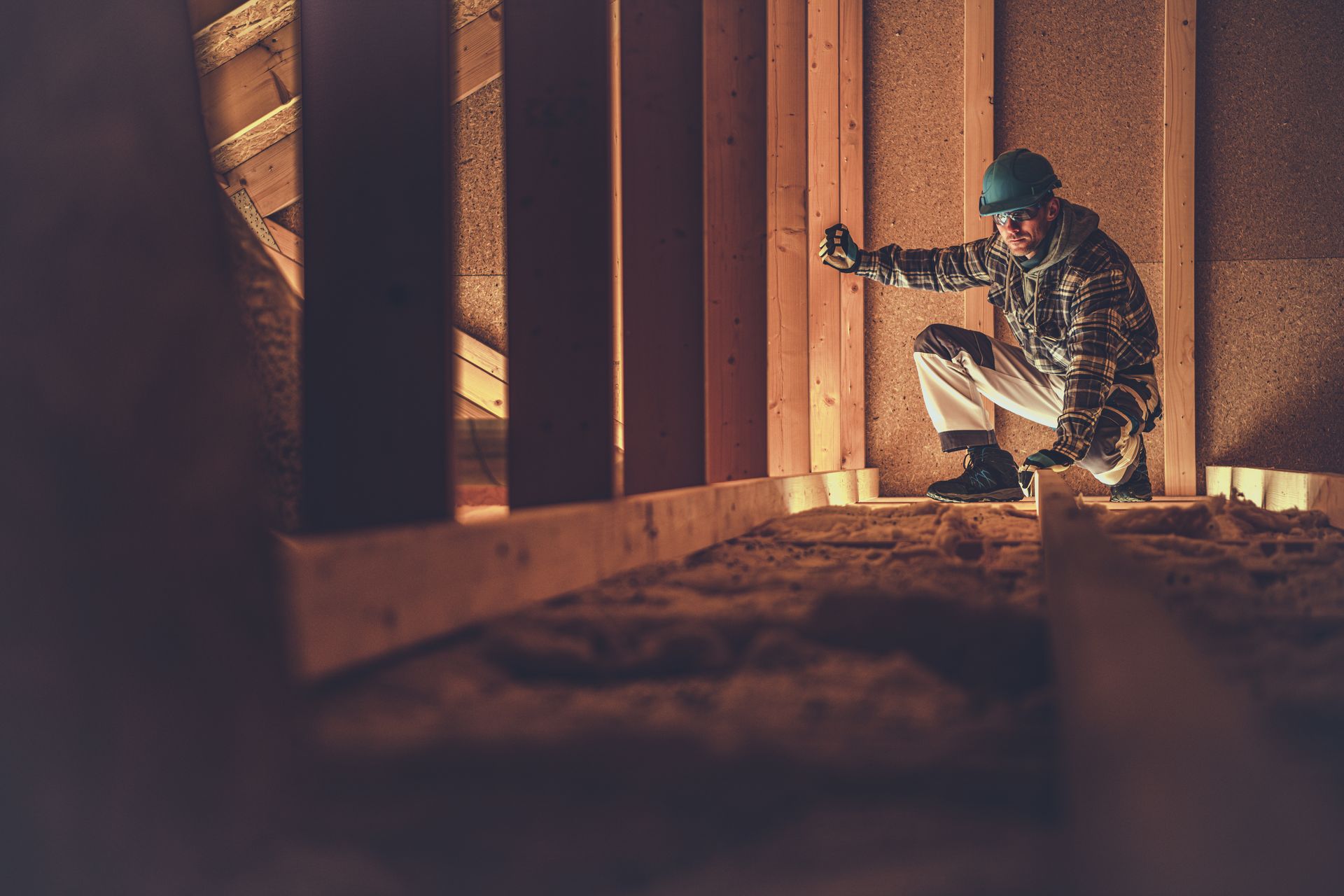 A person in camouflage crouches behind wooden slats, aiming a rifle in warm orange light.