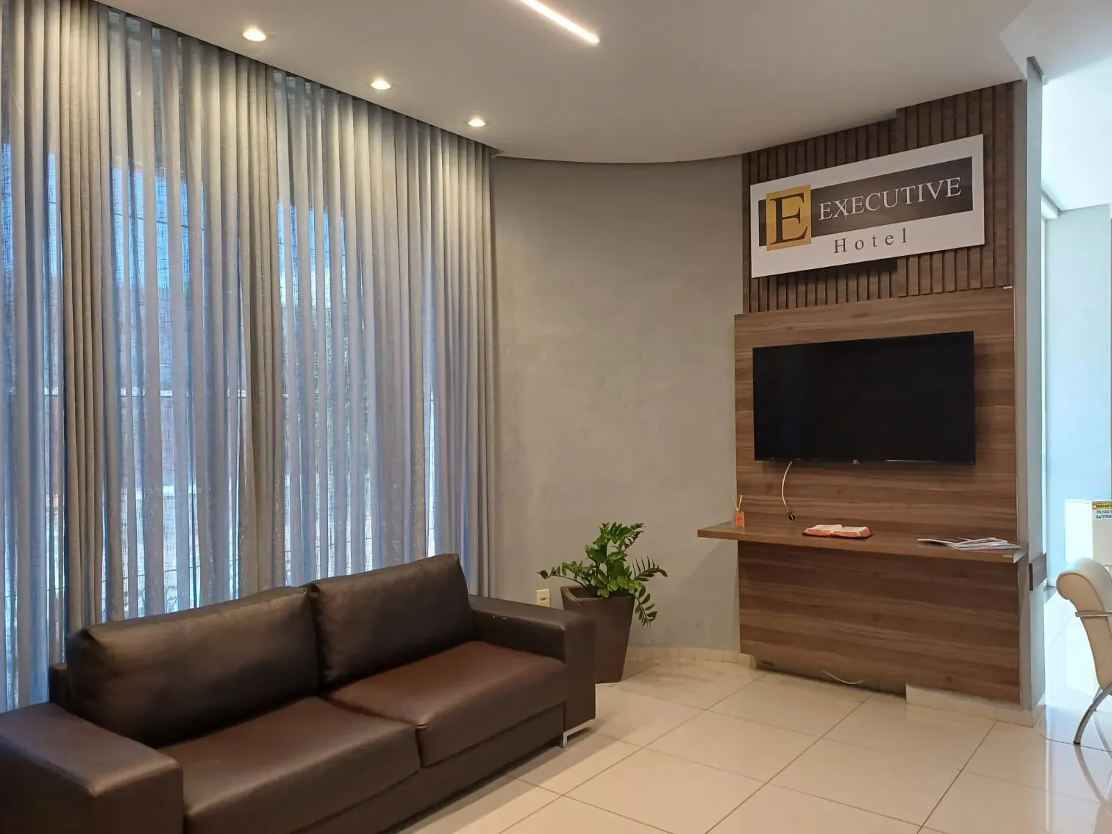 Uma sala de estar com um sofá marrom e uma TV de tela plana.-Executive-Hotel-MT