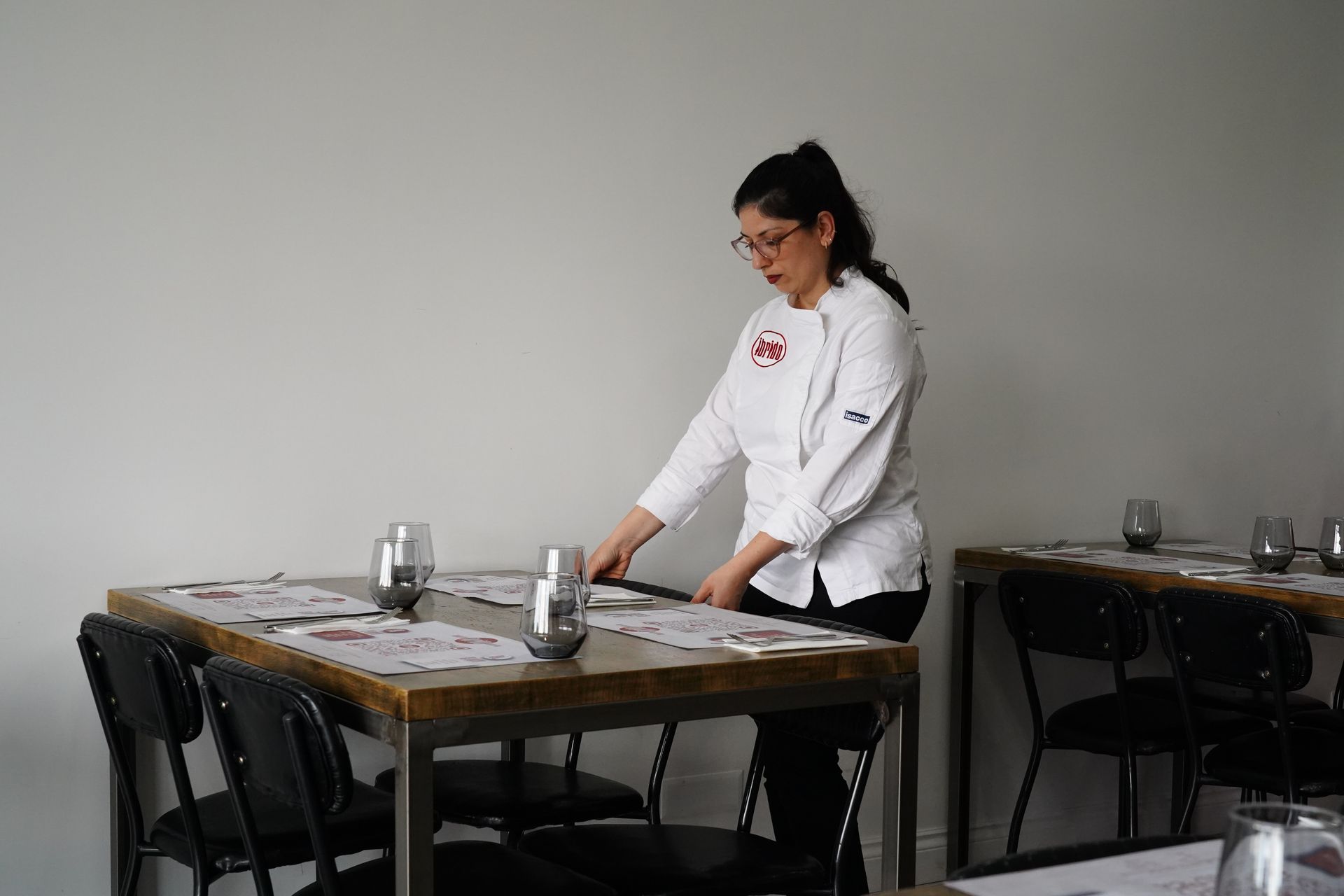 Una persona in camice bianco sistema degli oggetti su un tavolo in un ambiente simile a una sala da pranzo.