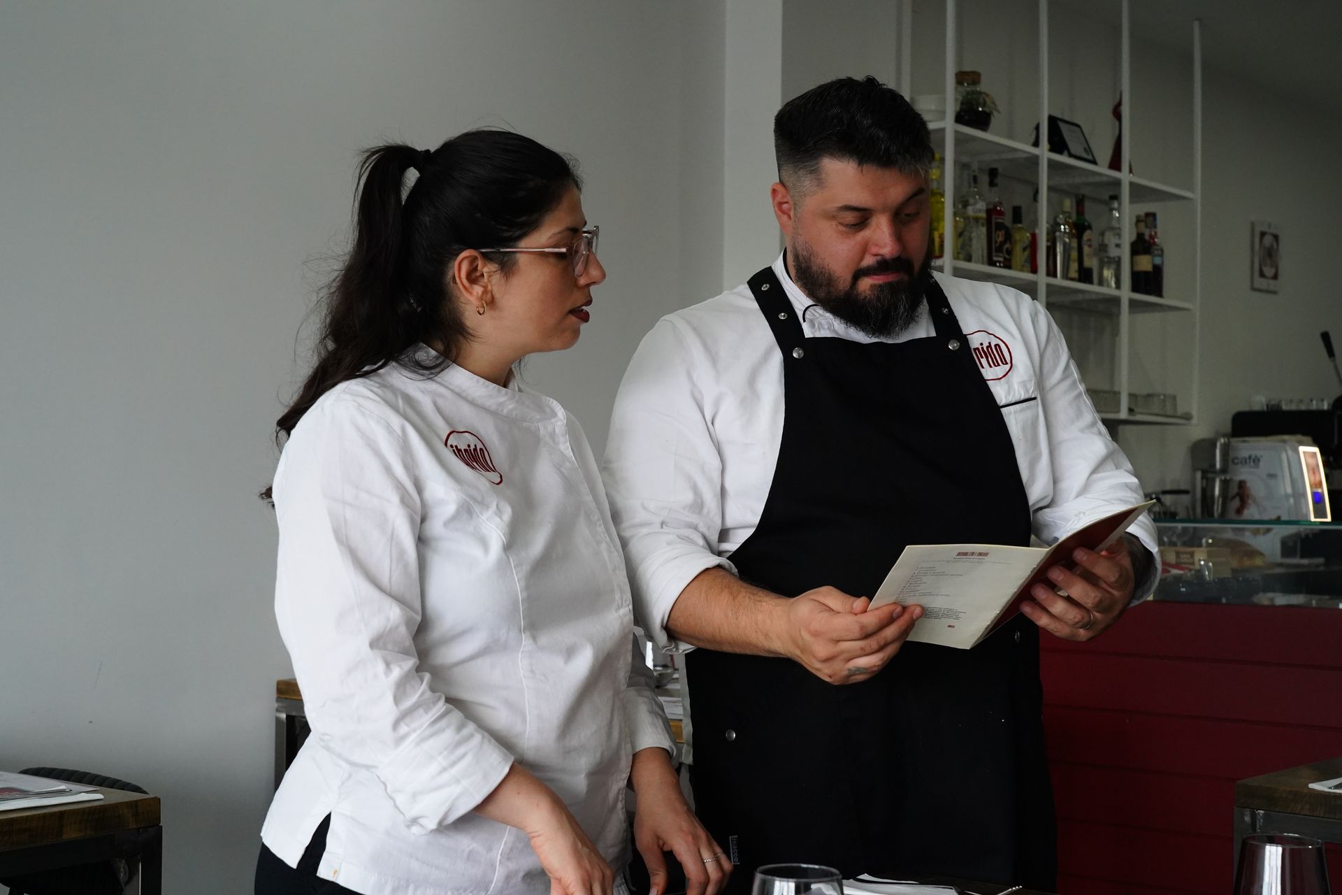 In cucina, due chef in camice e grembiule bianchi esaminano un menù.