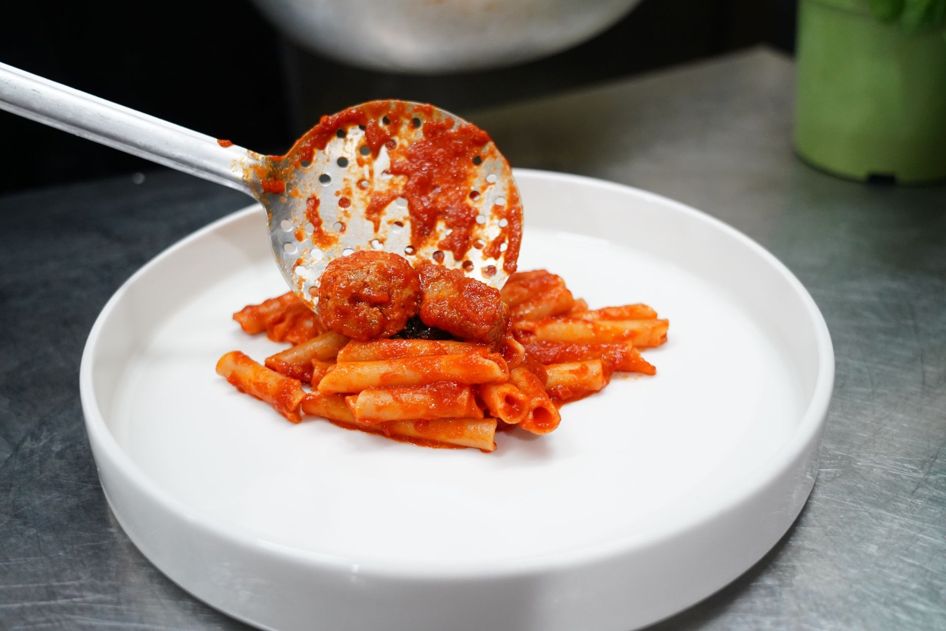 Penne al sugo di pomodoro su un piatto bianco, guarnite con formaggio grattugiato a cui un cucchiaio serve per aggiungerne altro.