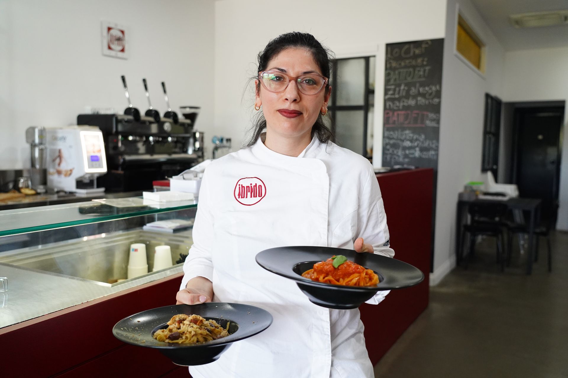 Uno chef in uniforme bianca tiene in mano due piatti di cibo nella cucina di un ristorante.
