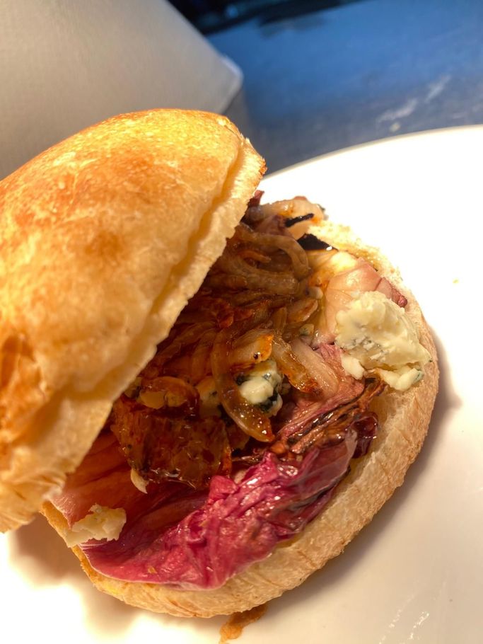 Panino aperto con carne sfilacciata e insalata di cavolo viola su un piatto bianco.