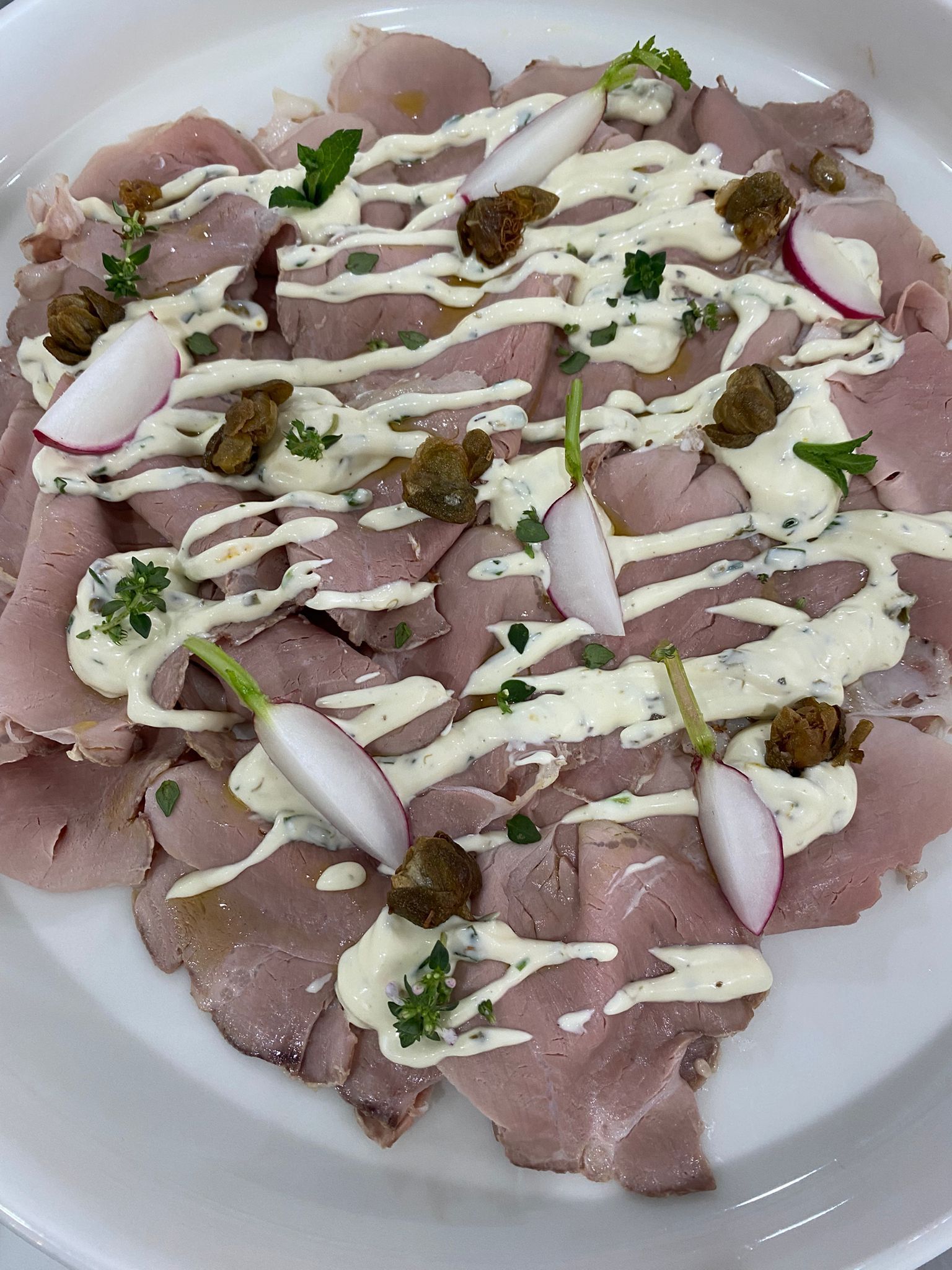 Carne affettata e impiattata, condita con salsa bianca, erbe aromatiche tritate e fettine di cipolla.