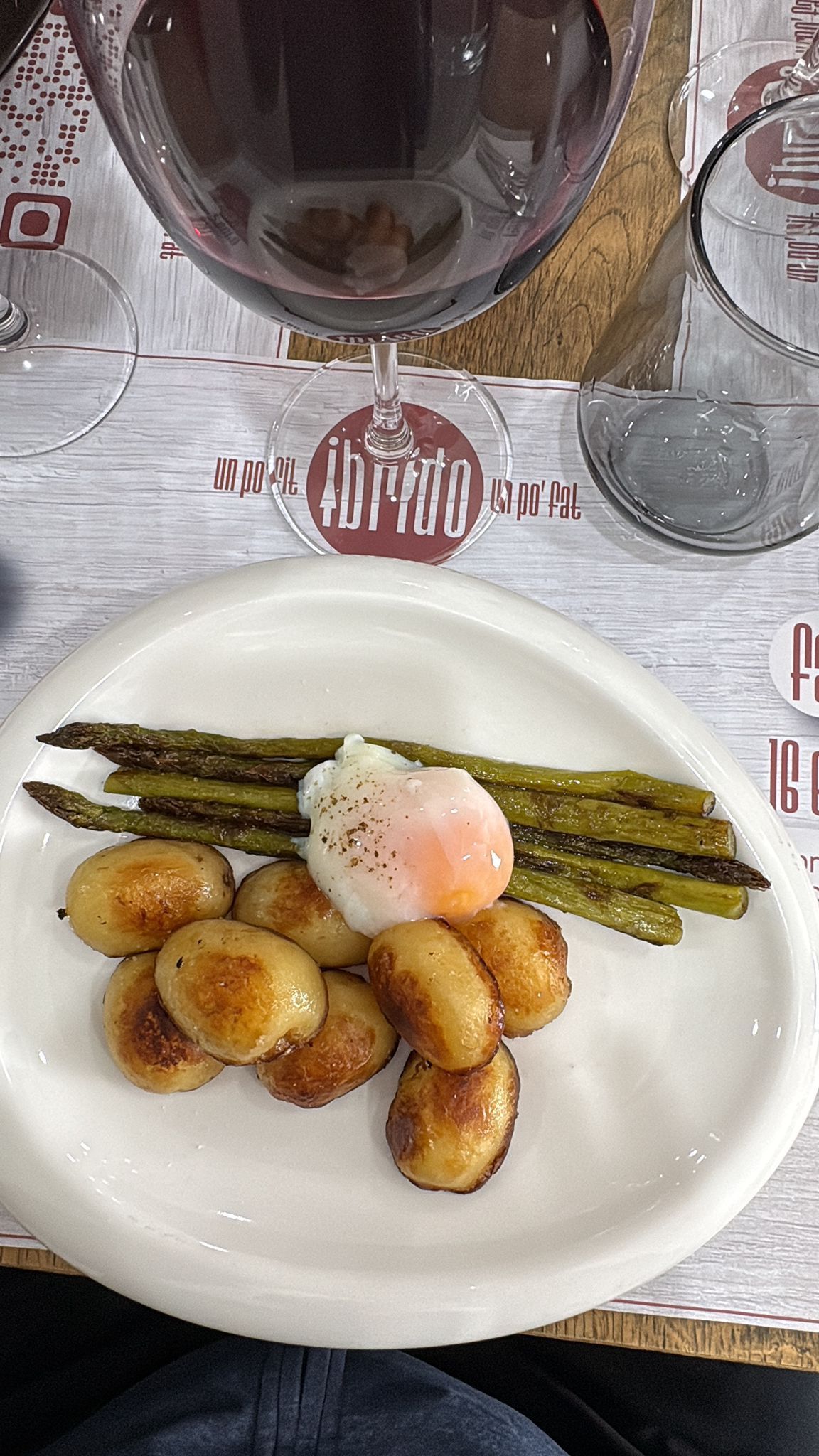Piatto con asparagi grigliati, patate arrosto e uovo in camicia su un tavolo di ristorante.