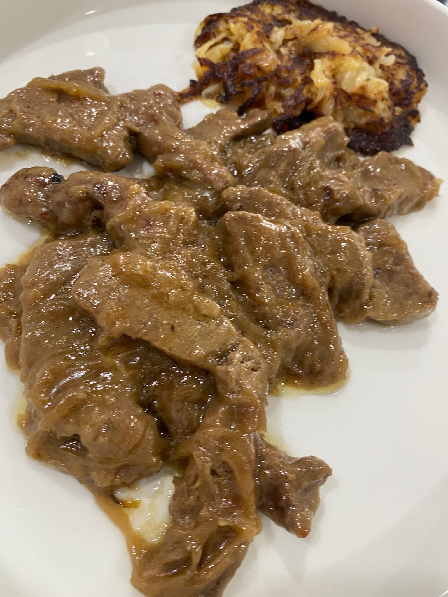 Piatto di carne brasata marrone con salsa e un piccolo spicchio di patata arrosto su un piatto bianco.