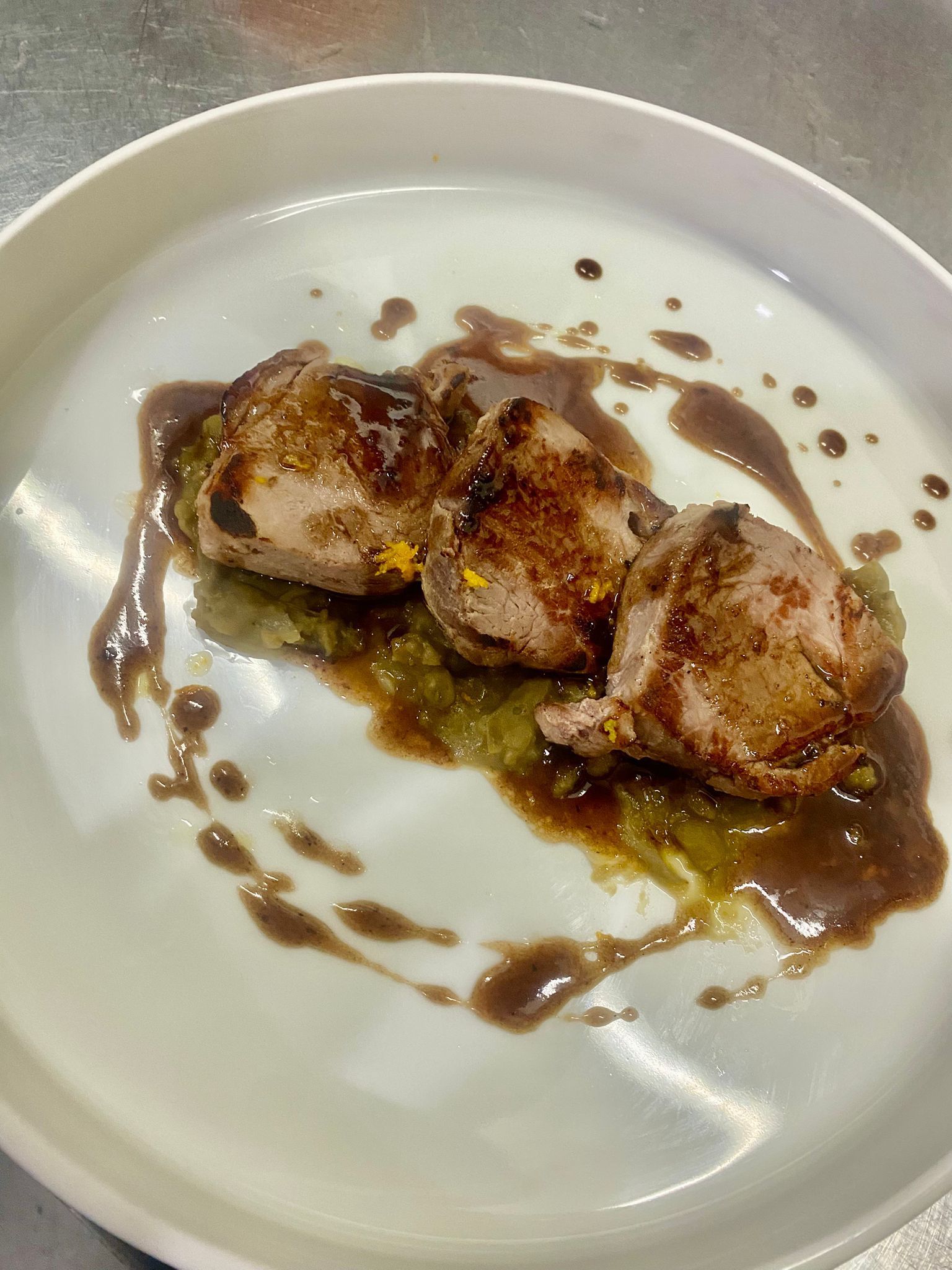 Tre capesante scottate su un piatto bianco con salsa marrone e un filo d'olio verde.