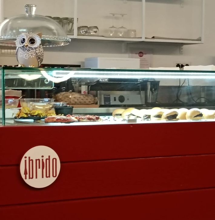 Un cappuccino bianco con decorazioni di latte art su un piattino, accanto a un croissant e un altro caffè su un tavolino del bar.