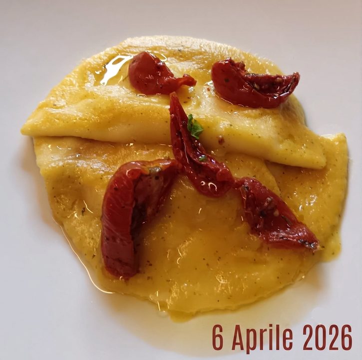 Polenta cremosa di colore giallo, guarnita con formaggio grattugiato e peperoni rossi arrostiti, servita su un piatto bianco.