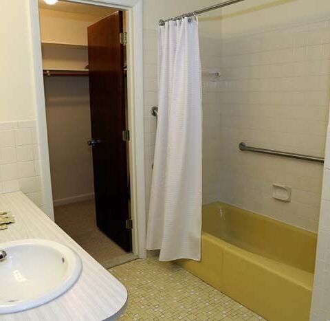 Bathroom with sink, shower curtain, and yellow bathtub beside an open closet door.