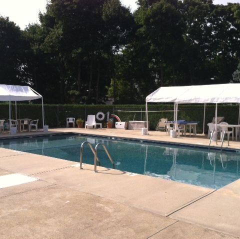 Outdoor swimming pool with white canopy tents and lounge chairs on a concrete deck, surrounded by trees