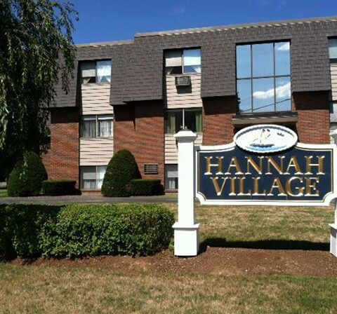 Hannah Village apartment sign in front of a brick residential building with hedges and windows