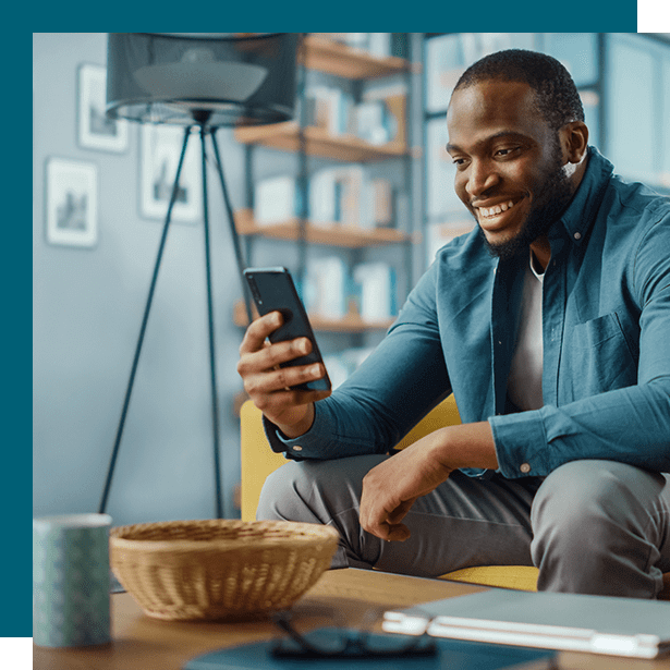 Man smiling while using a smartphone in a modern living room, seated beside a coffee table.