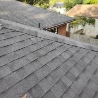 A high-angle view of gray asphalt roof shingles covering a residential roof, with a ridge cap running along the peak.
