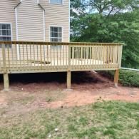 A newly built wooden deck with railings attached to the back of a light-colored, vinyl-sided house.
