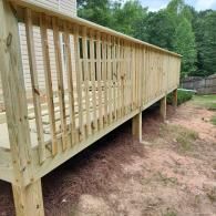 A newly constructed wooden deck featuring vertical railings and support posts, situated next to a light-colored house.