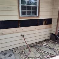 A house exterior with beige lap siding, where a section of board has been removed to reveal black moisture barrier.