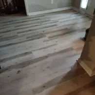 A close-up view of light gray, wood-look vinyl plank flooring installed in a room with white baseboards.