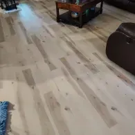Light-colored wood flooring with prominent knots and grain patterns in a living room with a coffee table and armchair.