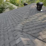 A gray asphalt shingle roof featuring a peaked hip joint and two black roof turbine vents.