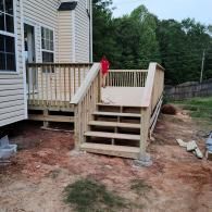 A newly constructed wooden deck and stairs attached to a beige house, with a person standing on the deck.