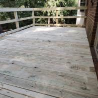 A newly constructed wooden deck featuring light-colored planks and a simple railing, positioned against a brick house.