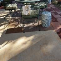 Outdoor patio with metal chairs, a round table, a blue and white ceramic stool, and a patterned rug on a concrete surface.