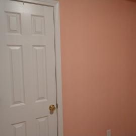 A white six-panel door with a gold knob set against a solid peach-colored wall.