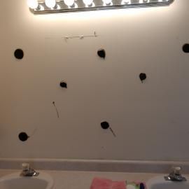 A bathroom wall with several black circular spots and marks where a mirror was removed below a vanity light fixture.
