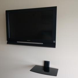 A black flat-screen TV mounted on a plain white wall above a small, black wall-mounted shelf.