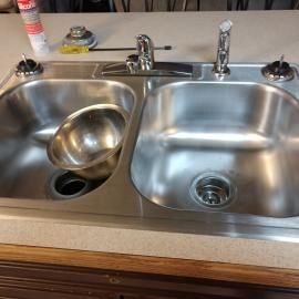A stainless steel double-basin kitchen sink with the faucet handles removed, sitting on a countertop.