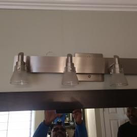 A three-bulb brushed-nickel bathroom vanity light fixture mounted above a mirror.
