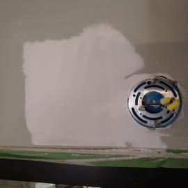 A wall patch with drywall compound and a metal electrical fixture mounted to the surface.