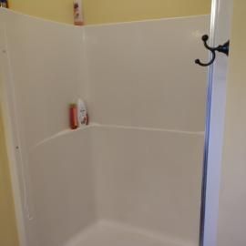 A white shower stall against yellow walls with a black robe hook mounted on the side panel.