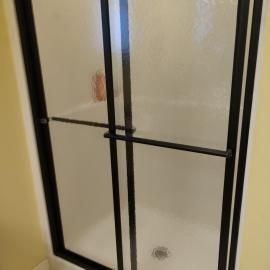 A walk-in shower with a white basin and translucent glass doors featuring a black metal frame.