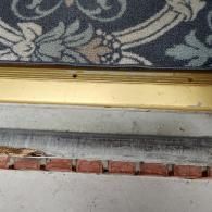 A close-up view of a door threshold, showing a gap between the gold metal saddle and the concrete step with red bricks.