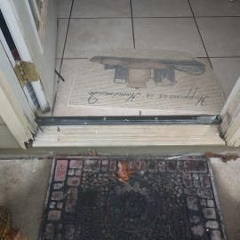 A doorway with a dark textured outdoor mat and an indoor mat reading 