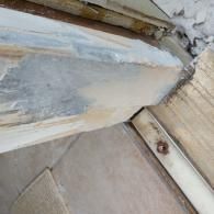 Close-up of a damaged, splintered wooden door threshold or frame with peeling light-colored paint over bare, aged wood.