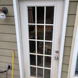 White paneled door with glass windows set in a wall with light tan horizontal siding and an exterior light fixture.