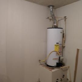 A white water heater stands in a corner with a vent pipe leading to the ceiling and connected plumbing.
