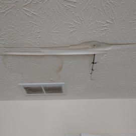 Water damage on a textured ceiling with a large crack, bubbling drywall, and brown water stains near an air vent.