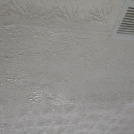 A textured white ceiling featuring a swirl pattern and a corner of a rectangular white air vent.