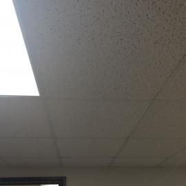 A white drop ceiling featuring a bright recessed light panel in the upper-left corner.