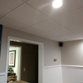 A view of a drop ceiling with a recessed light, leading into a doorway with a framed picture in the background.