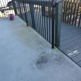 A concrete porch with rusted metal railing posts, adjacent to a gray wooden ramp section.