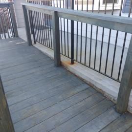 A wooden wheelchair ramp with a black metal railing leads up to a concrete landing against a building wall.