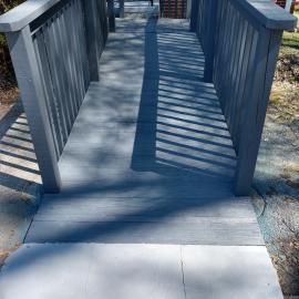 A ramp with gray wooden planks and railings leading to a transition area on a sunny day.