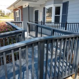 A gray wooden wheelchair ramp with black metal railings leading up to the entrance of a house.
