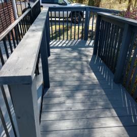 A gray wooden wheelchair ramp with dark metal railings leading outdoors towards a vehicle.