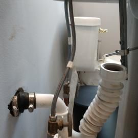 Plumbing pipes under a sink, featuring a flexible white drain hose and a wall-mounted pipe connection.